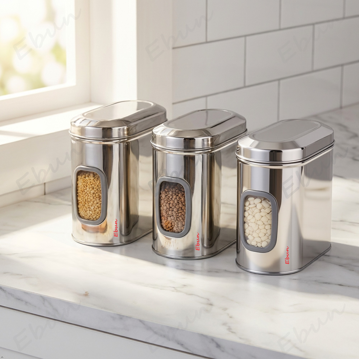Set of three Ebun stainless steel kitchen canisters on a marble countertop with visible brand name.