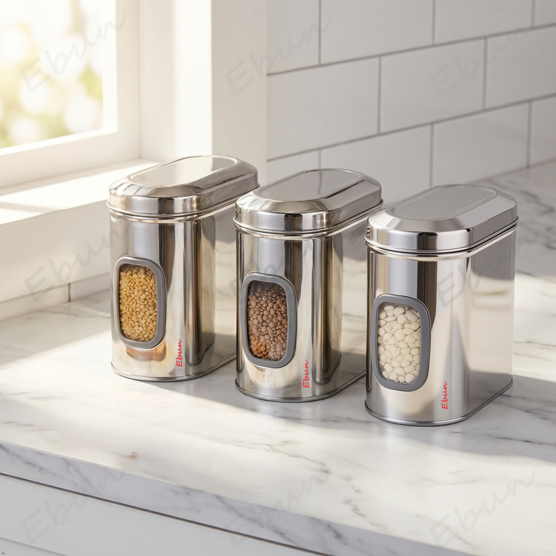Set of three Ebun stainless steel kitchen canisters on a marble countertop with visible brand name.