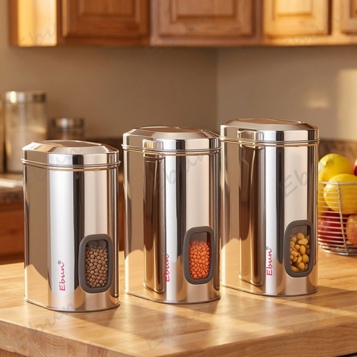 Three Ebun stainless steel kitchen canisters on a wooden countertop with a blurred background of a kitchen.